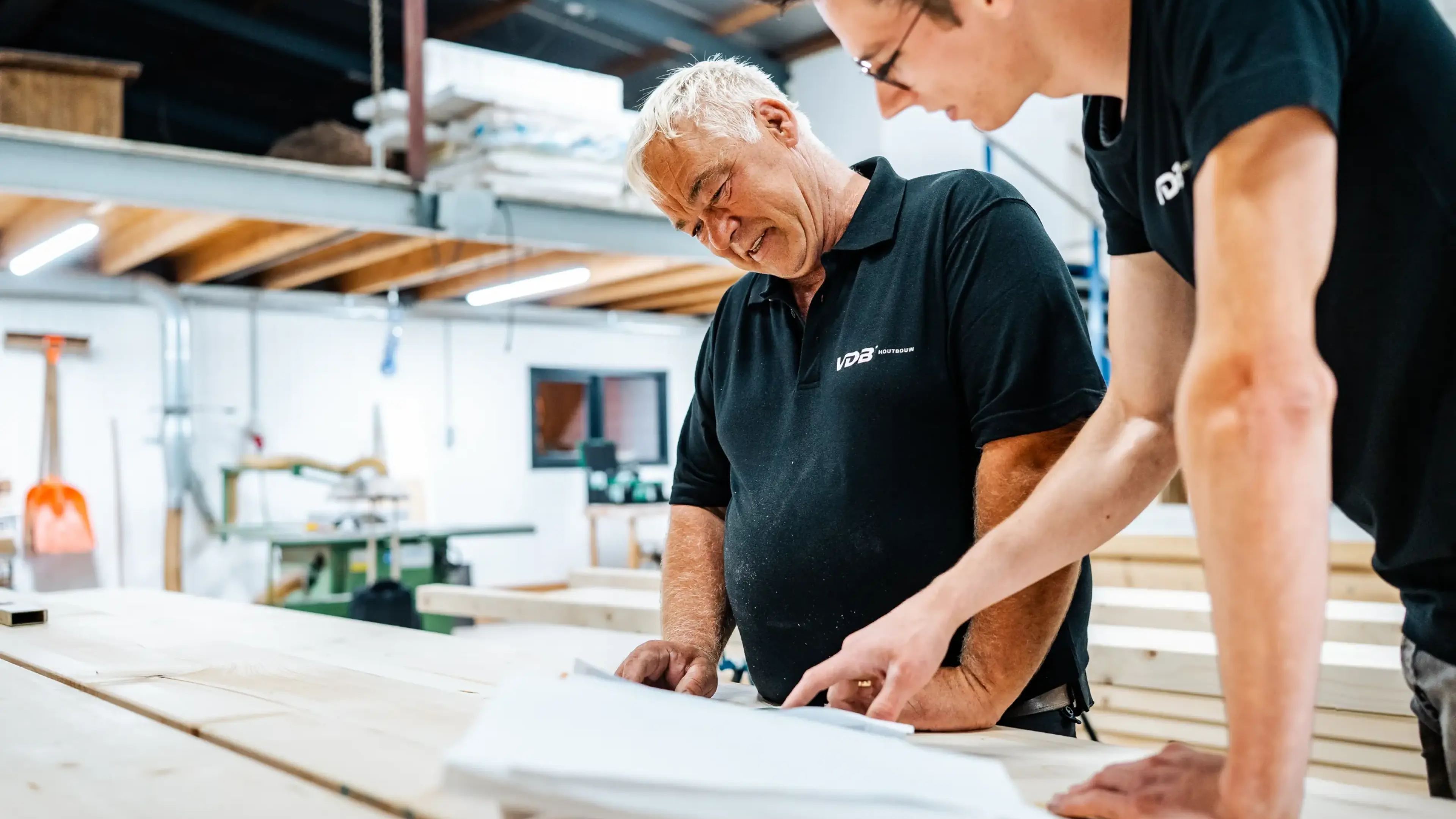 Twee vakmensen bekijken een bouwtekening in de werkplaats